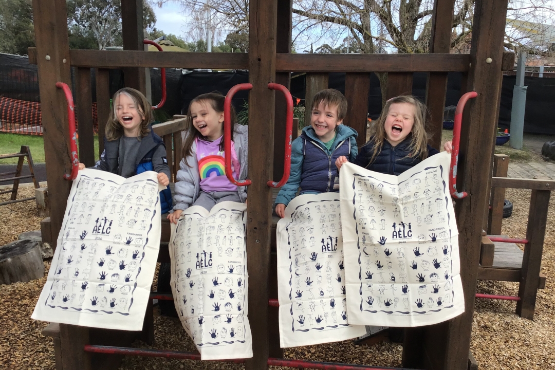 Children holding screen printed fundraising tea towels smiling in a playground