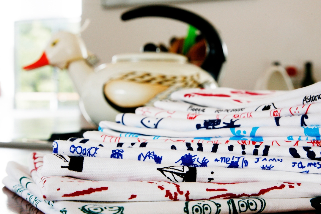 Printed school fundraising tea towels, stacked together in various colours