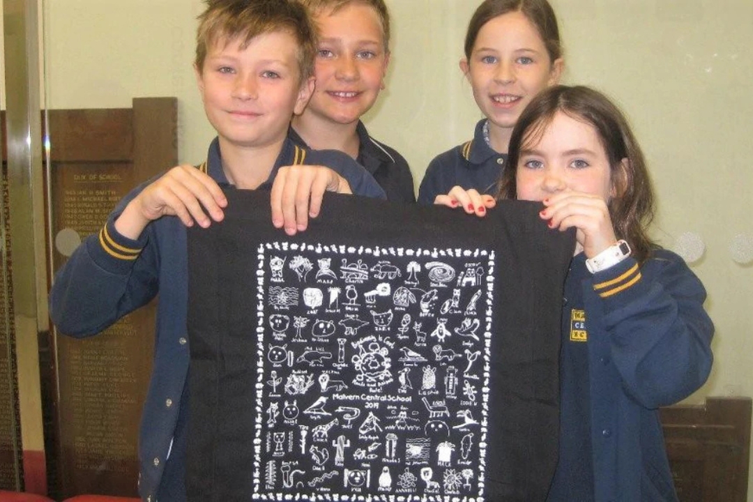 A group of smiling children proudly holding custom-printed tea towels, celebrating a successful school fundraiser organised by Expressions Australia.