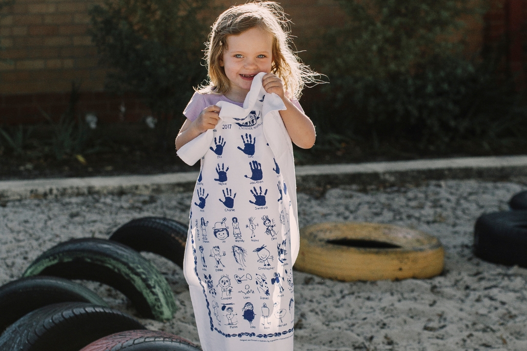 Child proudly holding custom-designed fundraising tea towels featuring student artwork