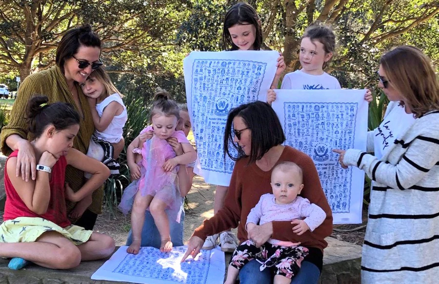 A group of women and children outdoors looking at personalised school tea towels from a past Expressions fundraiser.