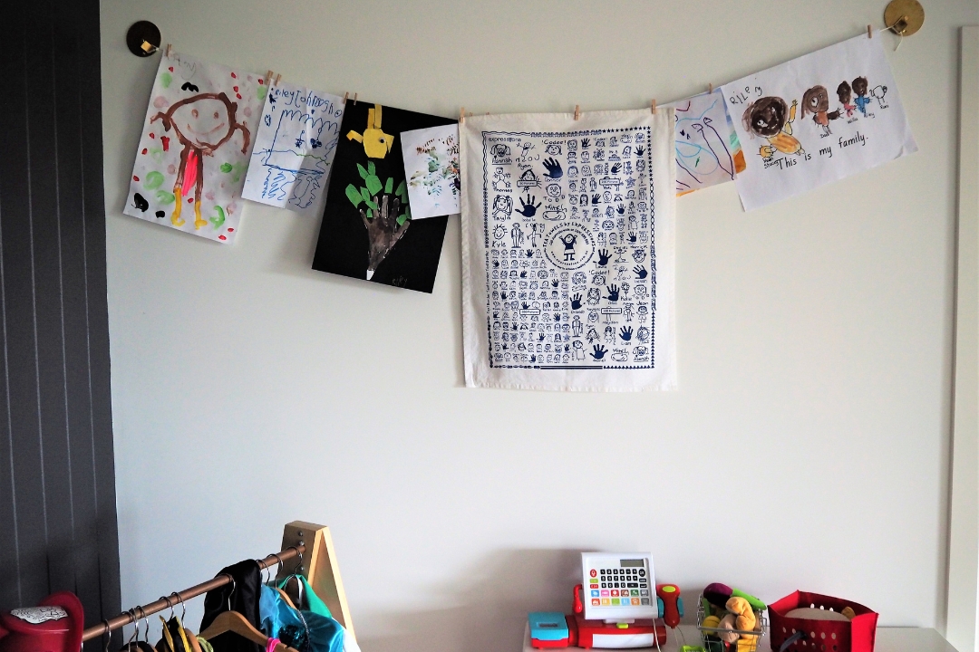School fundraising tea towel hanging on wall with child's drawings