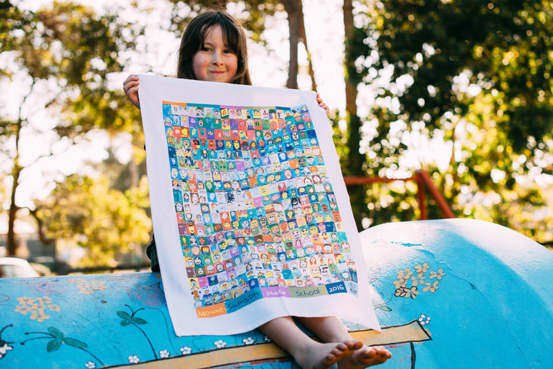 Children-designed tea towel fundraising product held by student