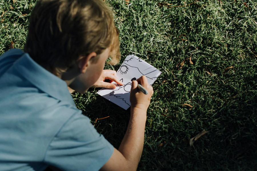 Child drawing on paper outdoors for tea towel fundraiser – capturing artwork for a school fundraising project run from home in Australia.