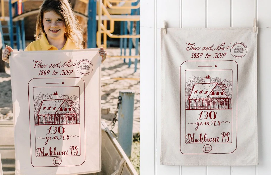 Child holding Blackburn Primary School 130th anniversary tea towel designed by students.