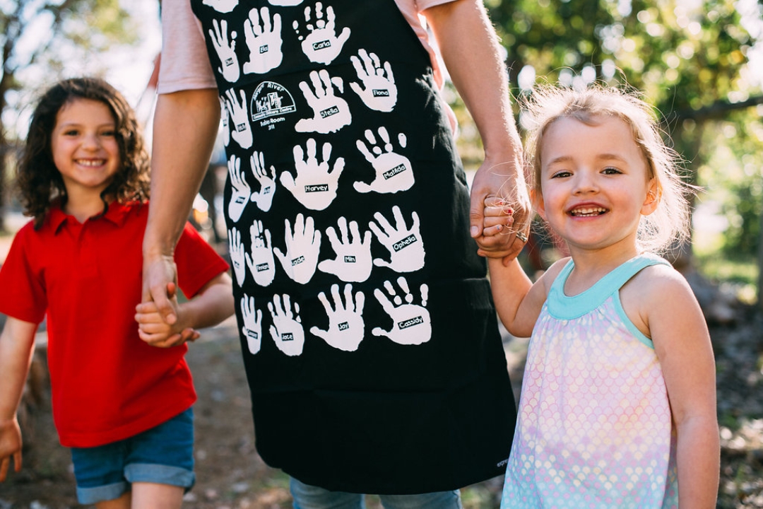 Children holding hands with mother wearing printed school fundraising apron