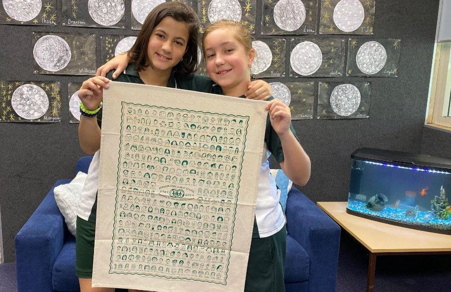 Two Edensor Park Public School students proudly holding their custom printed organic cotton tea towel fundraiser design for the school’s 30th anniversary.