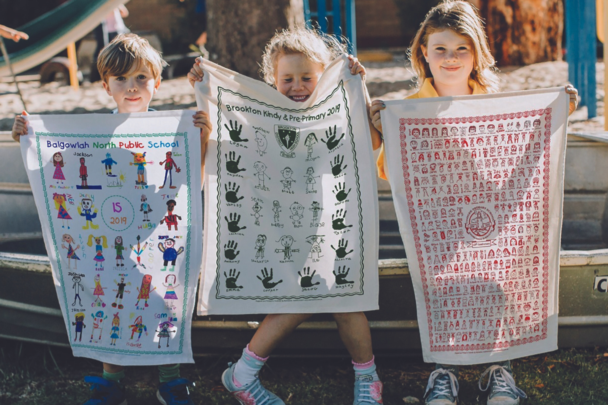 Children proudly holding personalised tea towels from Expressions school fundraising project