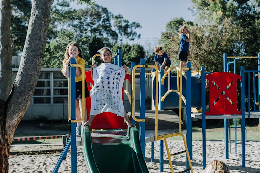 Children playing on a school playground, proudly displaying a tea towel printed with handprints and drawings from their Fundraiser Australia project by Expressions.