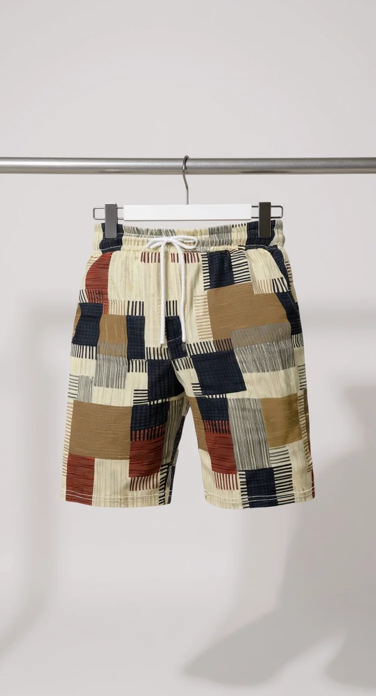 A pair of casual men's shorts hanging on a white plastic hanger against a plain light gray background. The shorts feature a geometric patchwork pattern with rectangular blocks in navy blue, tan, rust red, and cream colors. Each rectangle contains thin horizontal striped lines in various patterns within them. The shorts have an elastic waistband with a white drawstring closure. The fabric is a lightweight cotton material. The shorts are photographed straight-on, showing the full length from waist to hem. The image has a clean, minimalist studio lighting setup with subtle shadows cast on the gray backdrop.