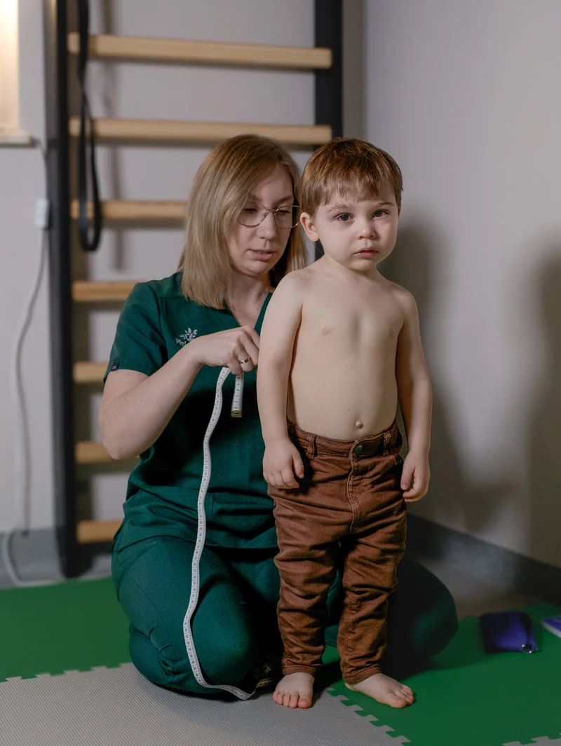 Fizjoterapeuta dziecięcy przeprowadza badanie postawy ciała u małego pacjenta podczas wizyty w gabinecie w Szczecinie.