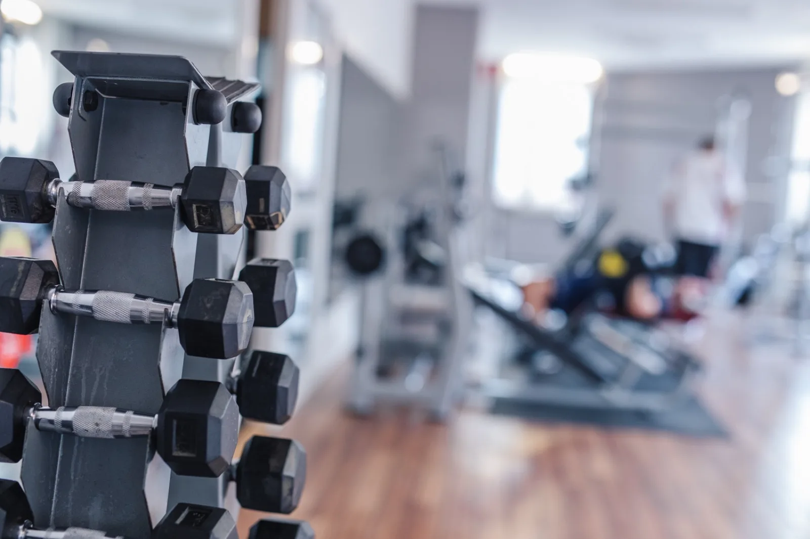 Hantelställ i förgrunden med gymmets maskiner bakom