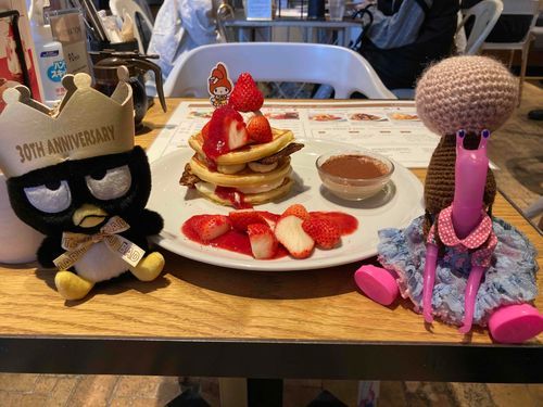 サンリオコラボメニューのパンケーキ♪
刺さってるピックのキャラはランダムで、飼い主のはマイメロちゃんだったよ。
ここのパンケーキは甘すぎなくて美味しいんだよね♪

あっ！この日の目的はパンケーキじゃなくて、ばつ丸くんの隣にいる足つきカタツムリ人の真っ白いお家に色を塗るというワークショップに参加することだったんだよね。行く前に背負ってるのは、飼い主が適当に編んだ桜の木だけど、帰ってきた時には素敵なお家を背負ってたんだよ♪
今度機会があれば紹介するね〜♪