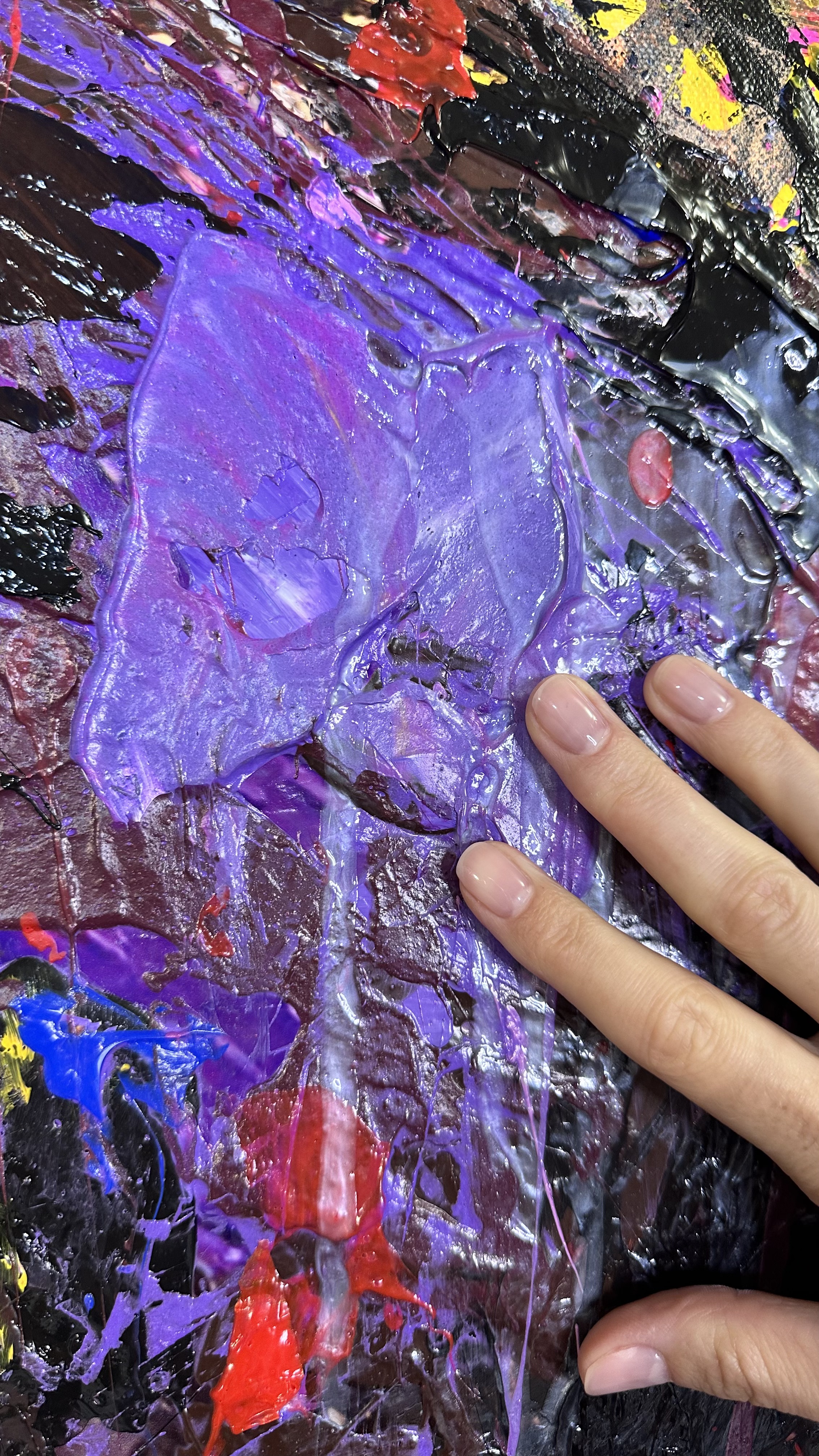 A close-up of Raging Torrent by Gabrielle Benot: thick ridges of purple and violet paint over deep red, with the artist's fingertips resting on the surface for scale.