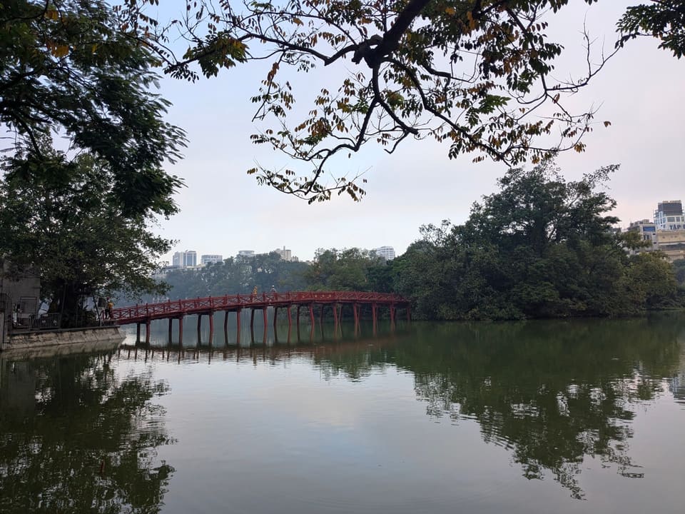 Red bridge crossing Hoan Kiem Lake beneath mature trees