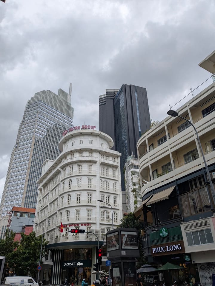 Historic white corner building beneath modern towers in Ho Chi Minh City