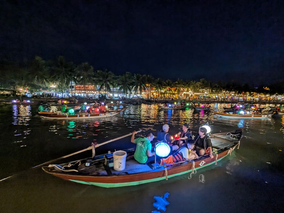 Small illuminated boats moving across the river in Hoi An
