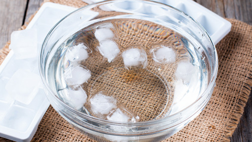 Glass bowl filled with ice water on a jute mat, used for face icing and cold plunge therapy