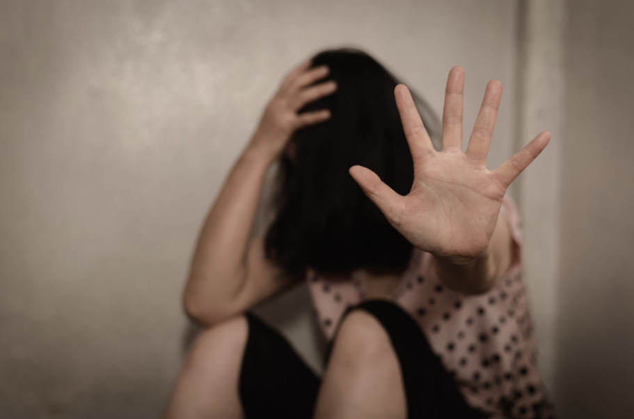 Distressed woman sitting against a wall with hand raised to signal stop, symbolizing trauma and emotional distress