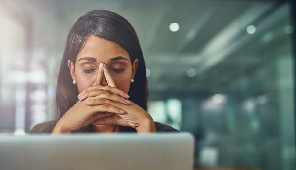 Woman sitting at her desk, appearing exhausted and sad while working intently on her laptop, illustrating the hidden struggle of high-functioning depression—balancing productivity with emotional distres