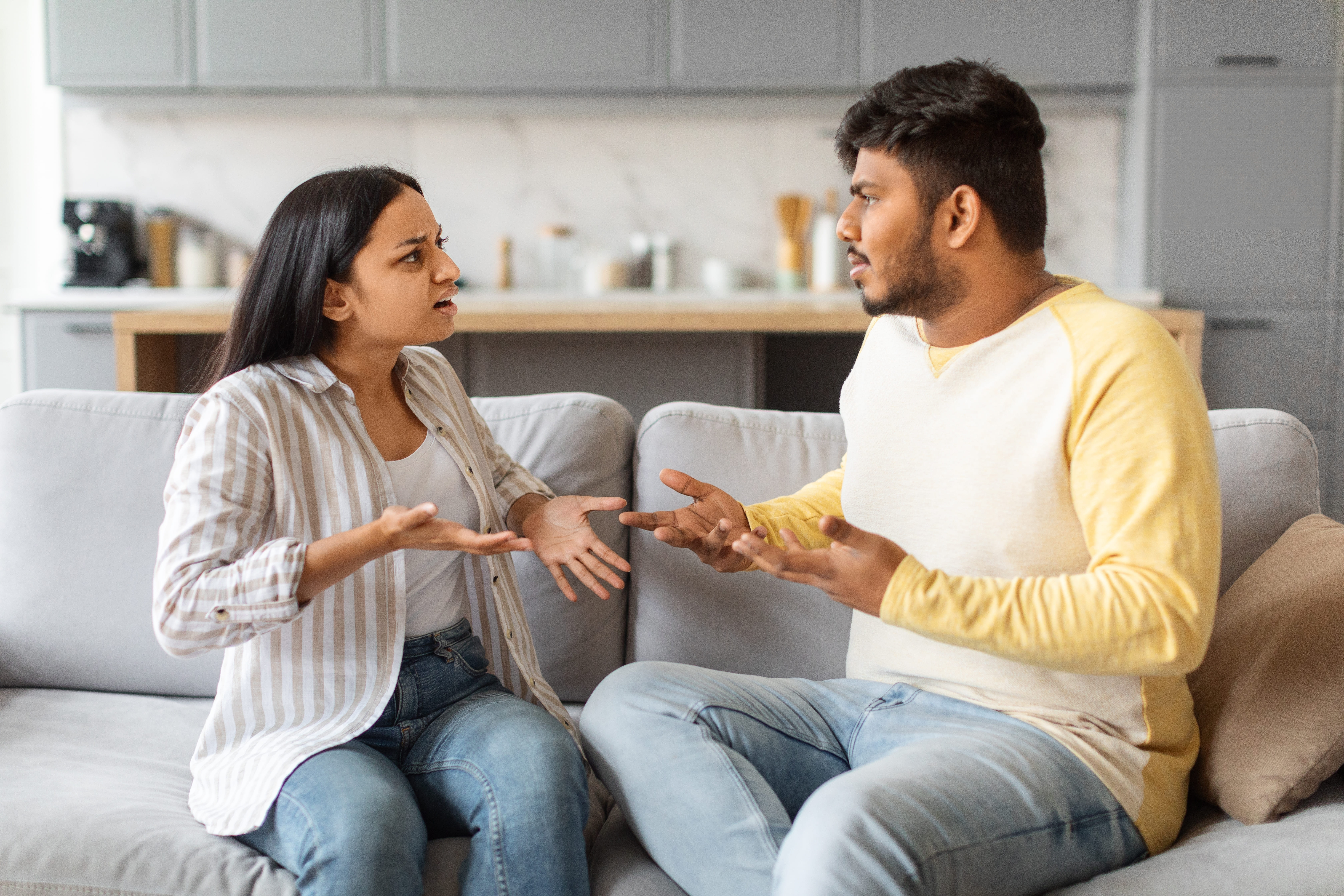 Indian couple sitting apart on a sofa looking upset after a fight, symbolizing tension and misunderstanding in relationships