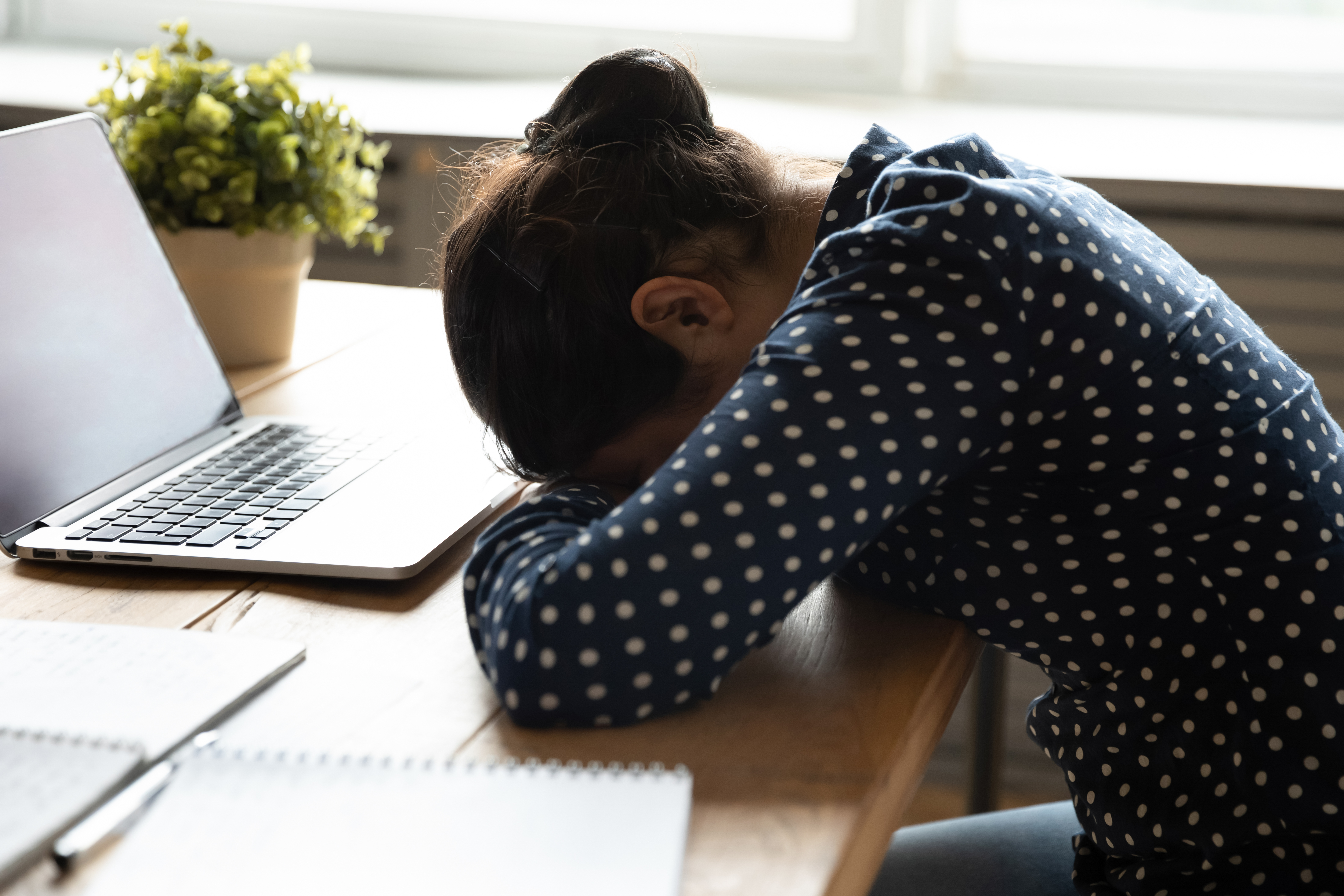 A tired woman sitting at her desk with eyes closed and head resting on hand, representing constant fatigue despite rest – why I feel tired all the time