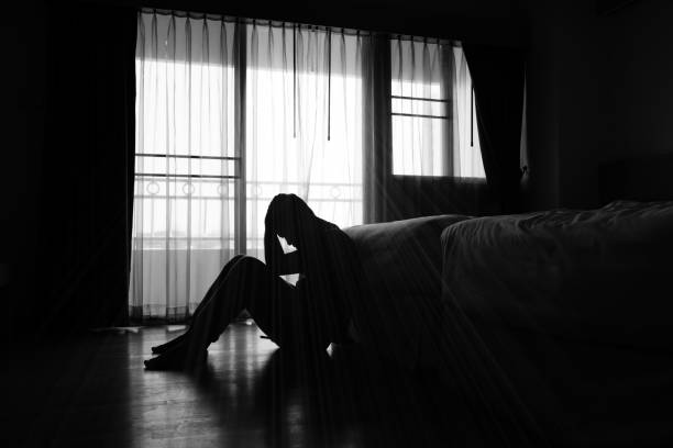 Silhouette of a person sitting on the floor in a dark room, holding their head in distress, symbolizing  depression.