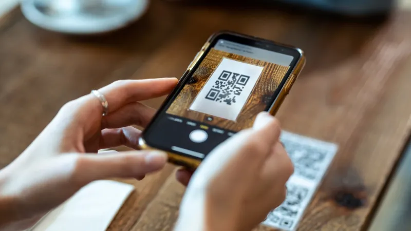 Cartel turístico con código QR impreso en una plaza histórica, con el destino al fondo levemente desenfocado