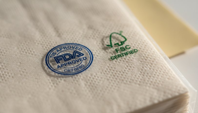 Close-up of a paper napkin with an FDA approved and FSC certified logo visible on the packaging.