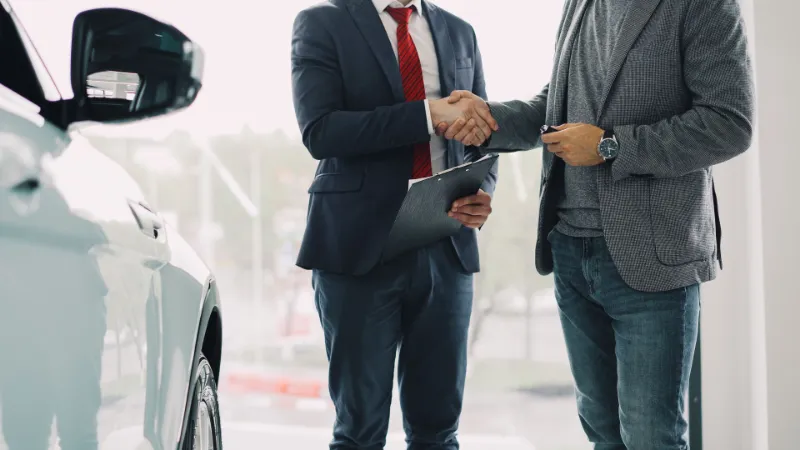 Dos personas cerrando el contrato de alquiler junto a un auto