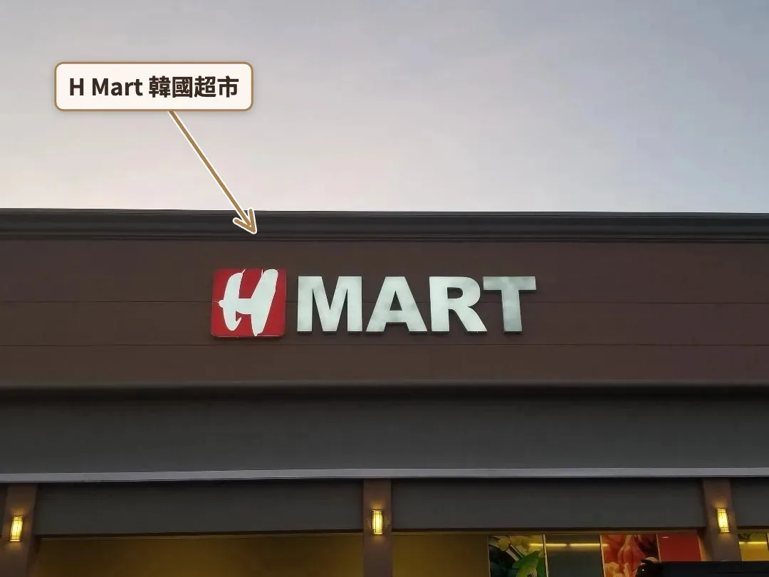 黃昏天空下的咖啡色建築外牆，掛著紅底白字 H MART 招牌
