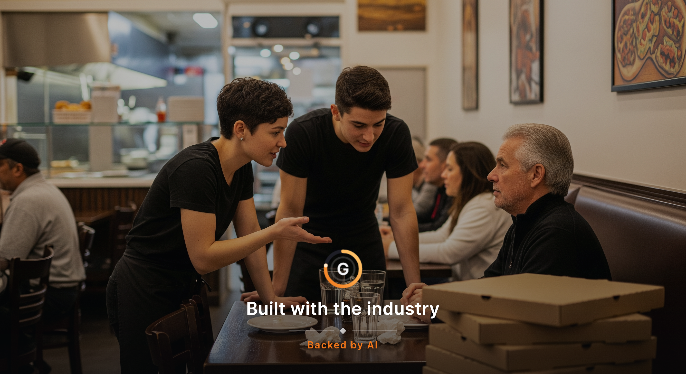 A server at a small pizza restaurant leans slightly toward a seated regular, one hand open in explanation while a manager steps in beside them to quietly clarify the check, with pizza boxes, water glasses, and the low glow of dinner service around them. Candid, mid-conversation, no one looking at th