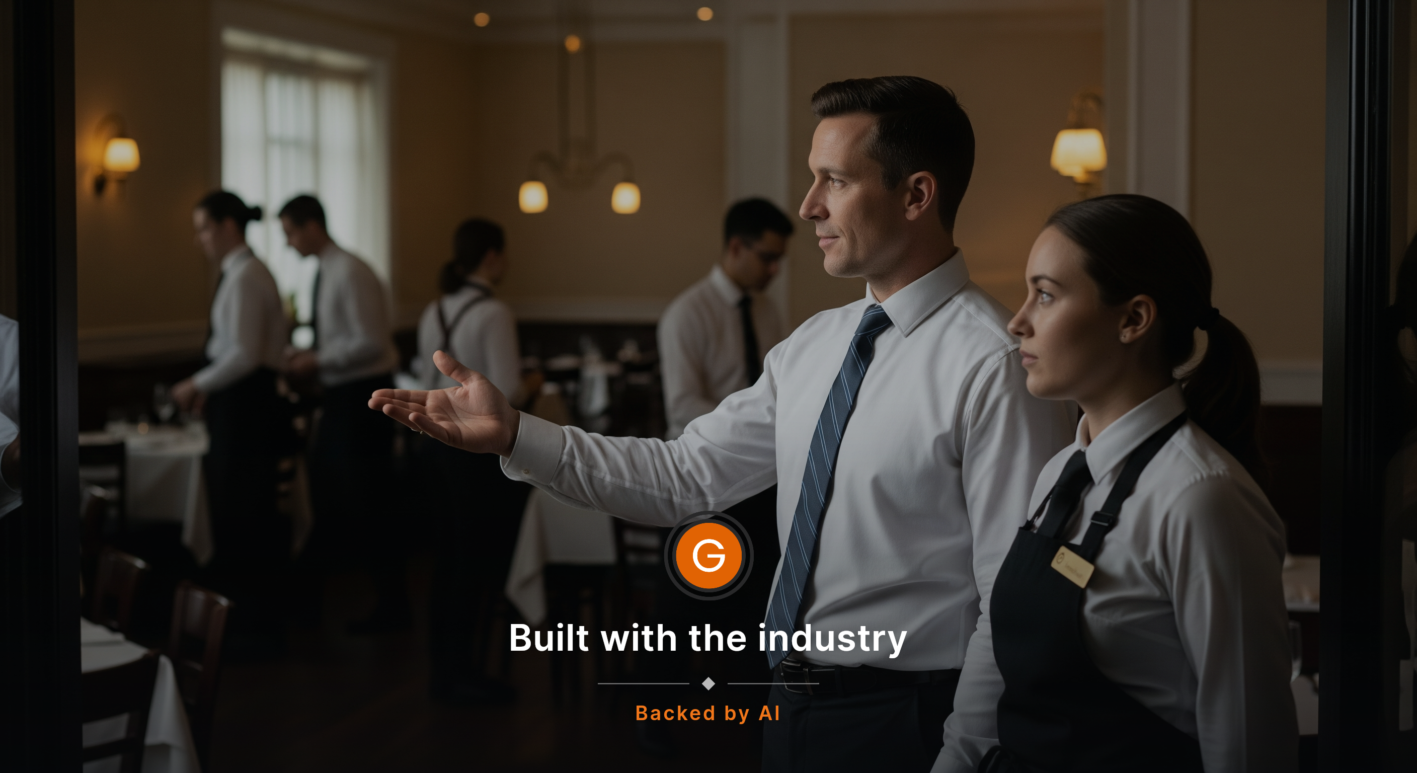 A floor manager and a new host stand just off the entrance during pre-shift, the manager quietly gesturing with an open hand toward the dining room while the host follows the room with focused eyes, servers and bussers moving in the background as the team gets set for service. Candid, documentary st