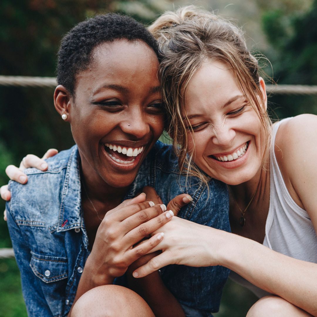 Two female friends laughing and cuddling outside.