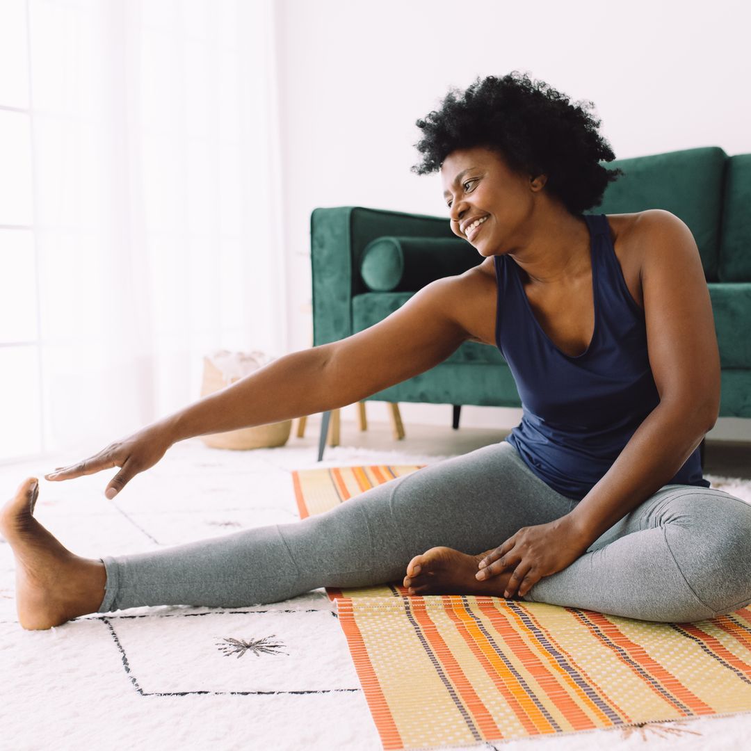A smiling woman on the floor doing stretching exercises.