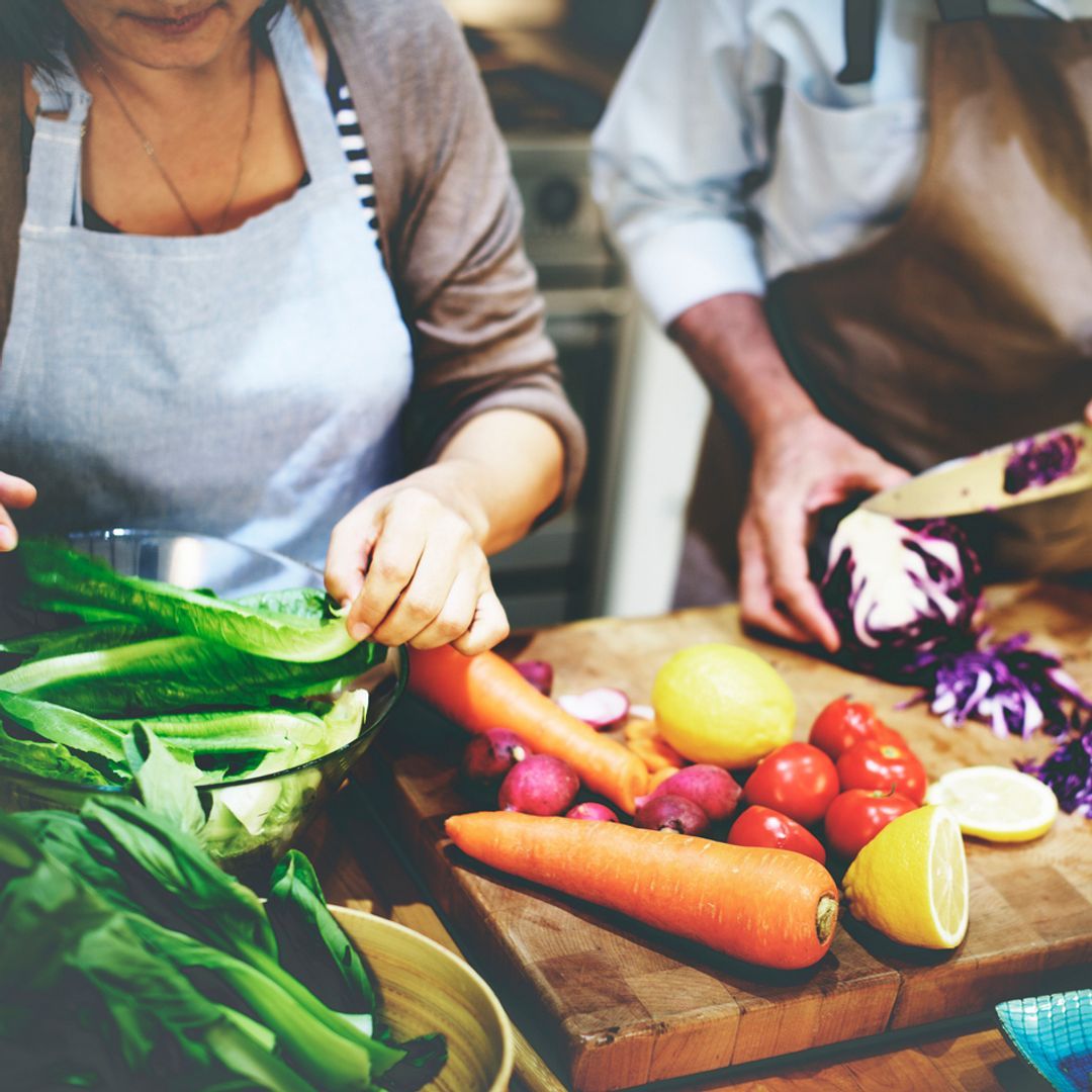 A couple preparing vegetables on a large wooden chopping board.