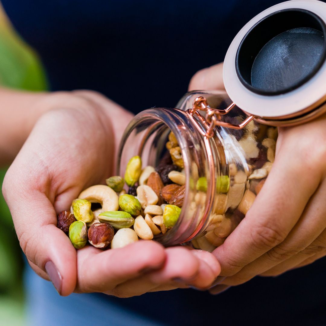 A hand holding a hermetic glass pot with mixed nuts being tipped out