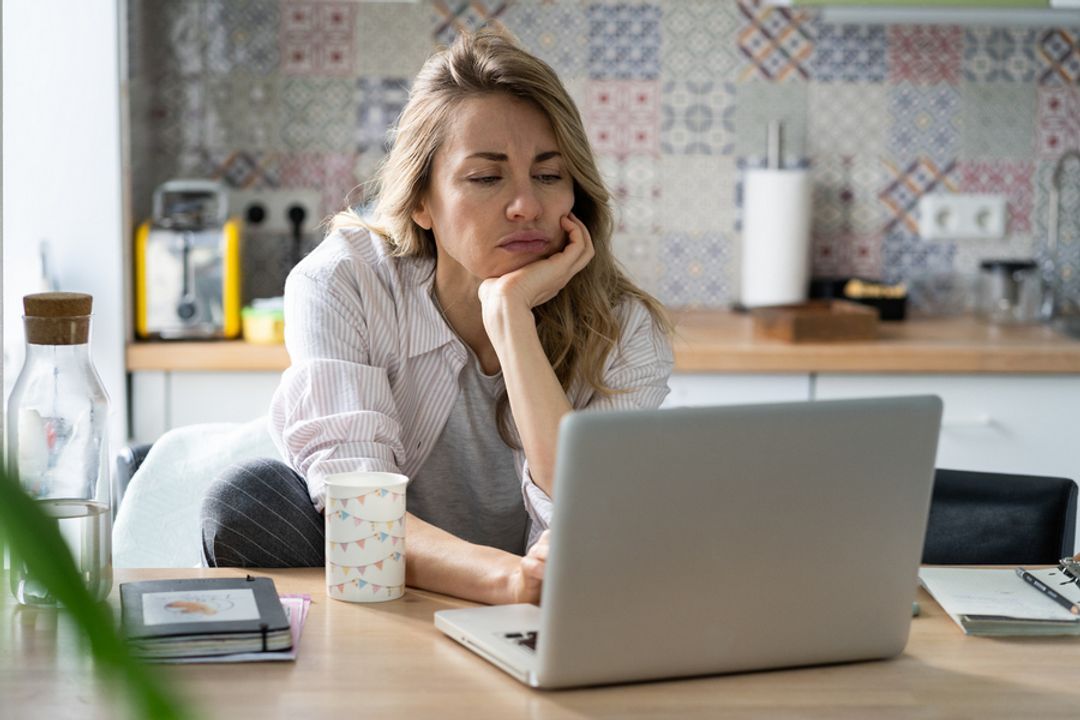 Woman on her laptop in the kitchen looking perplexed.