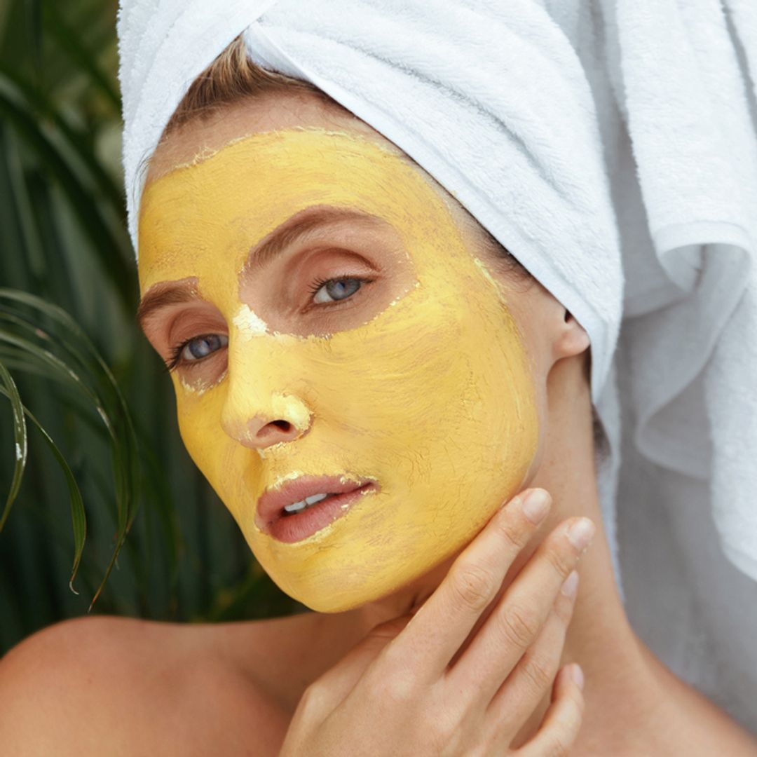 Portrait of women with hair in a bath towel and face covered with yellow skincare product.