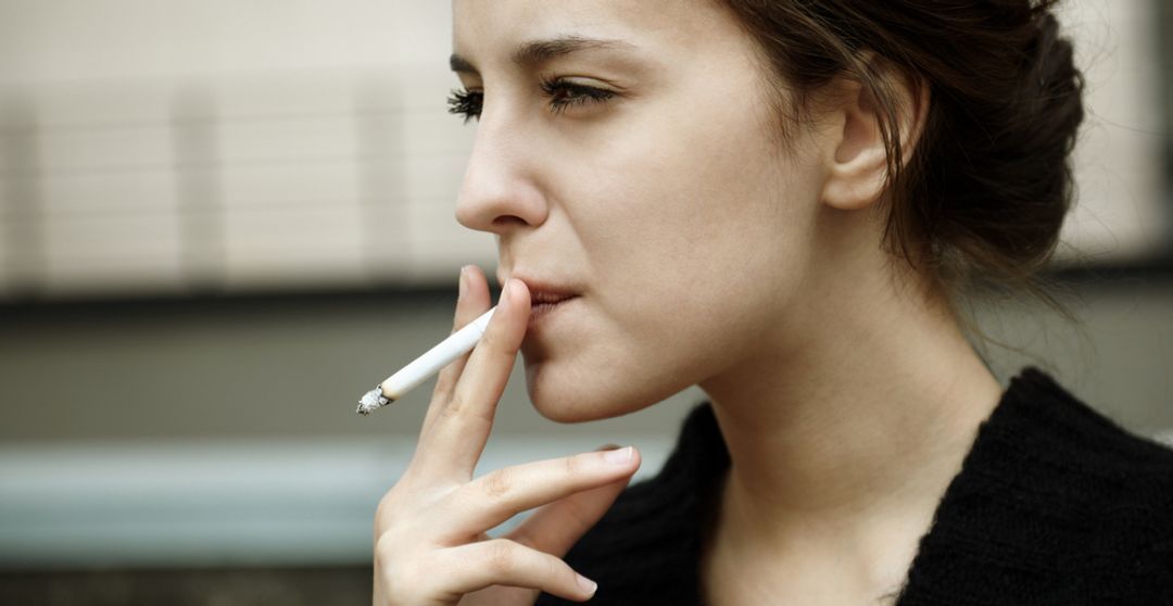 Woman smoking a cigarette outside while staring into space.