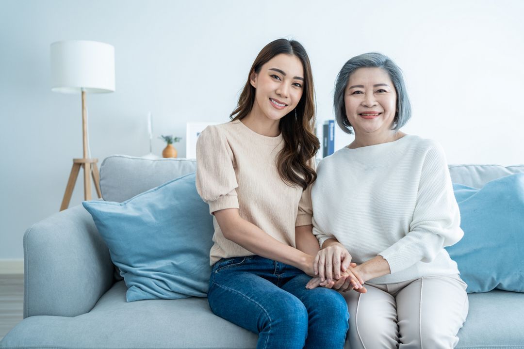 Mother and daughter sitting together on a sofa smiling and holding hands.   