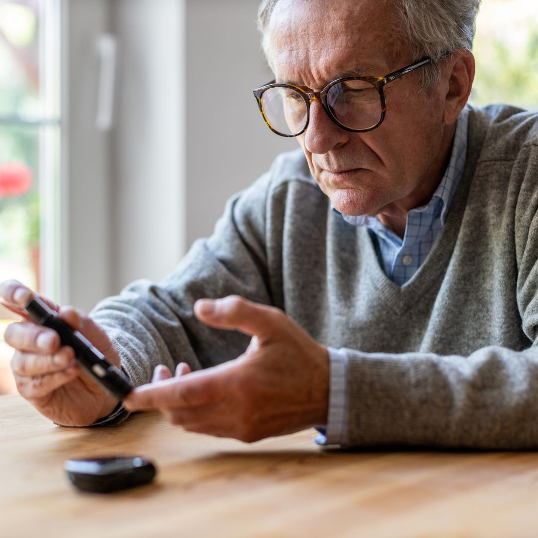 Man sitting at a table checking his blood sugar levels using a Glucometer.