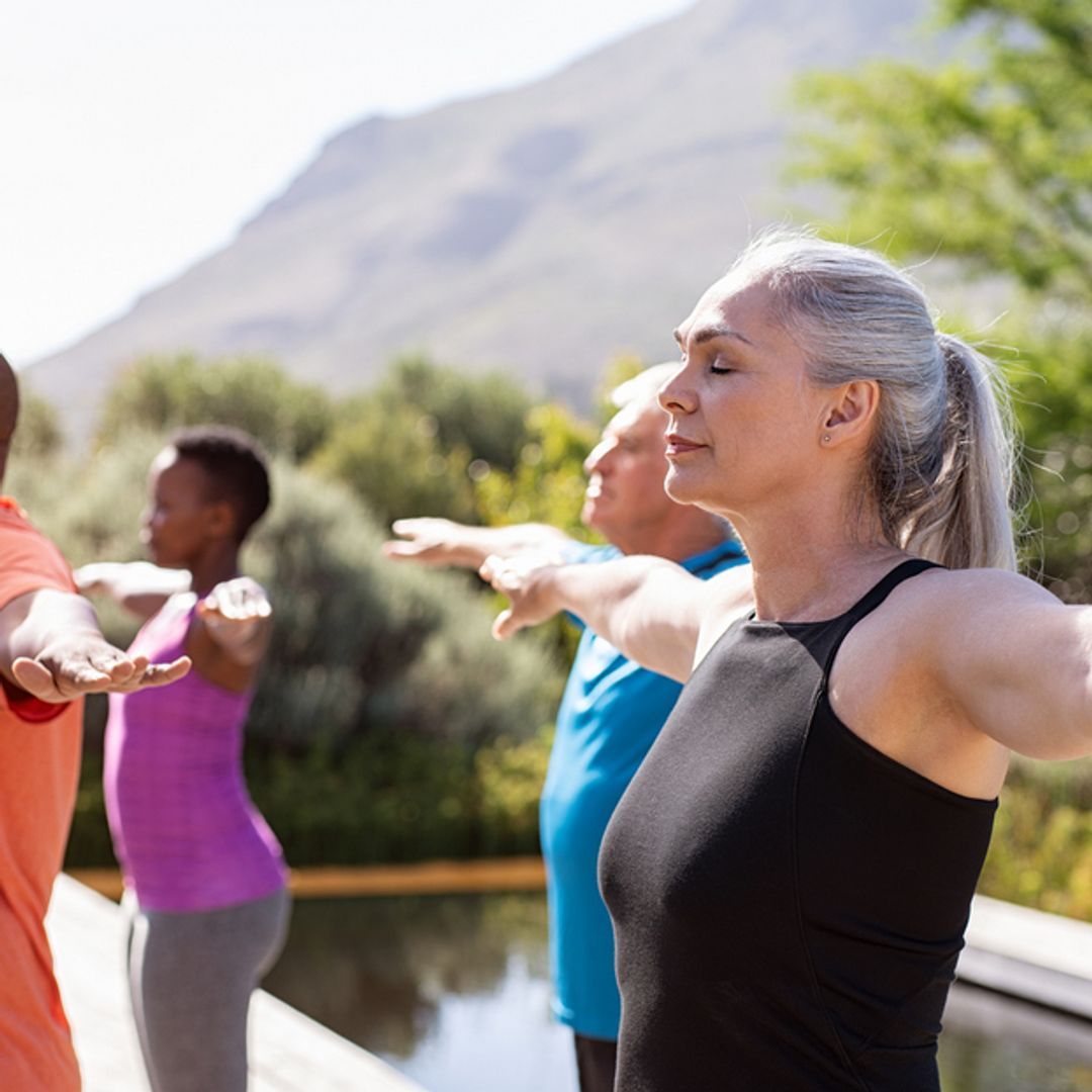 Group of mature people doing exercise outside by a pool.