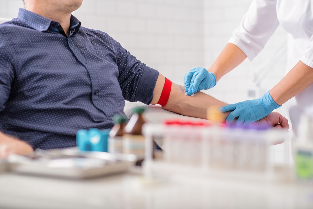 Man in a blue shirt having a blood test in a clinical setting.