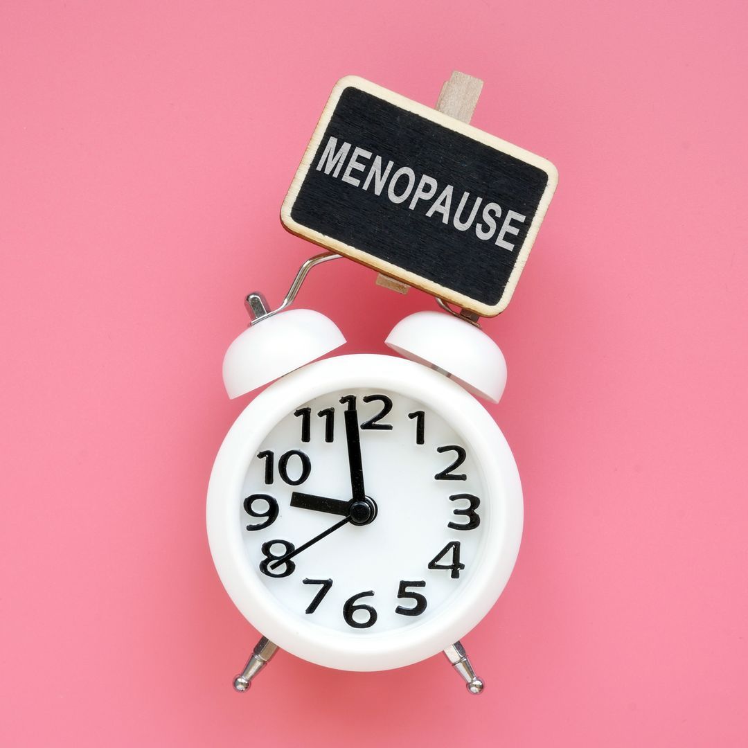 The word menopause on top of an alarm clock on a pink background