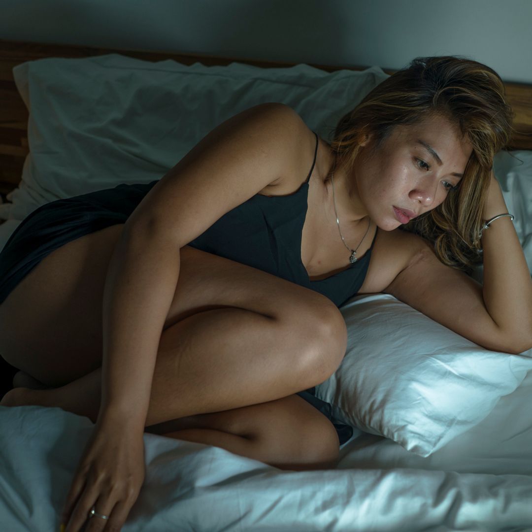 A woman in a nightgown lying on a bed feeling sad.