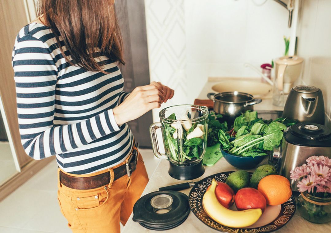 A woman in her kitchen preparing the ingredients for a healthy fruit and vegetable smoothie.