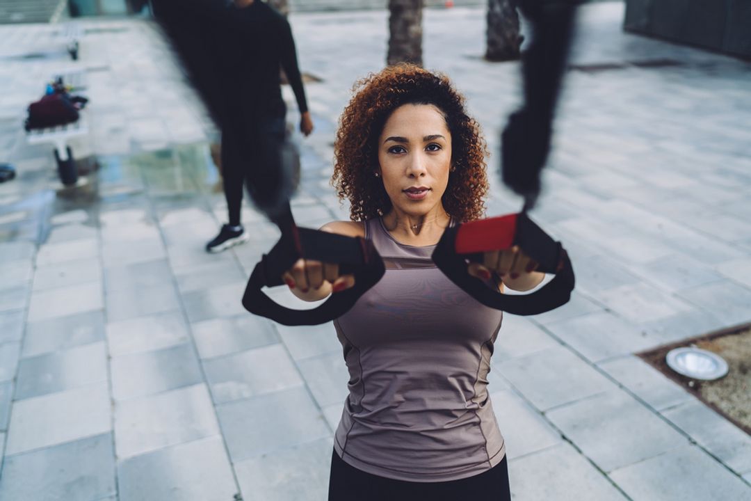 Determined woman looking straight ahead doing chest exercises outside.