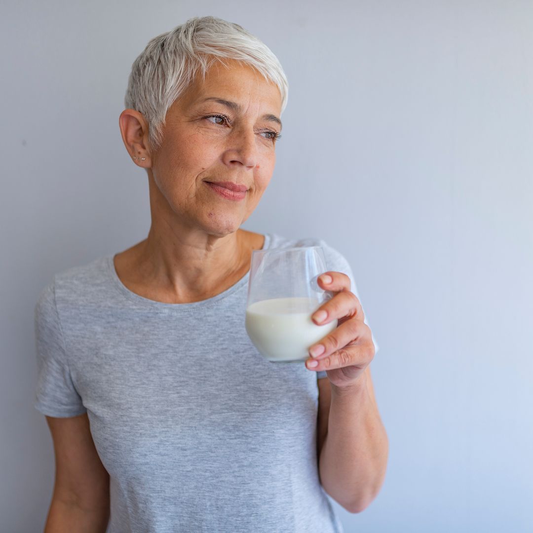 A woman drinking a glass of milk with a grey background.