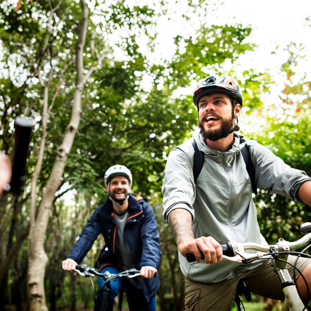 A group of friends on bikes riding through the woods smiling. 